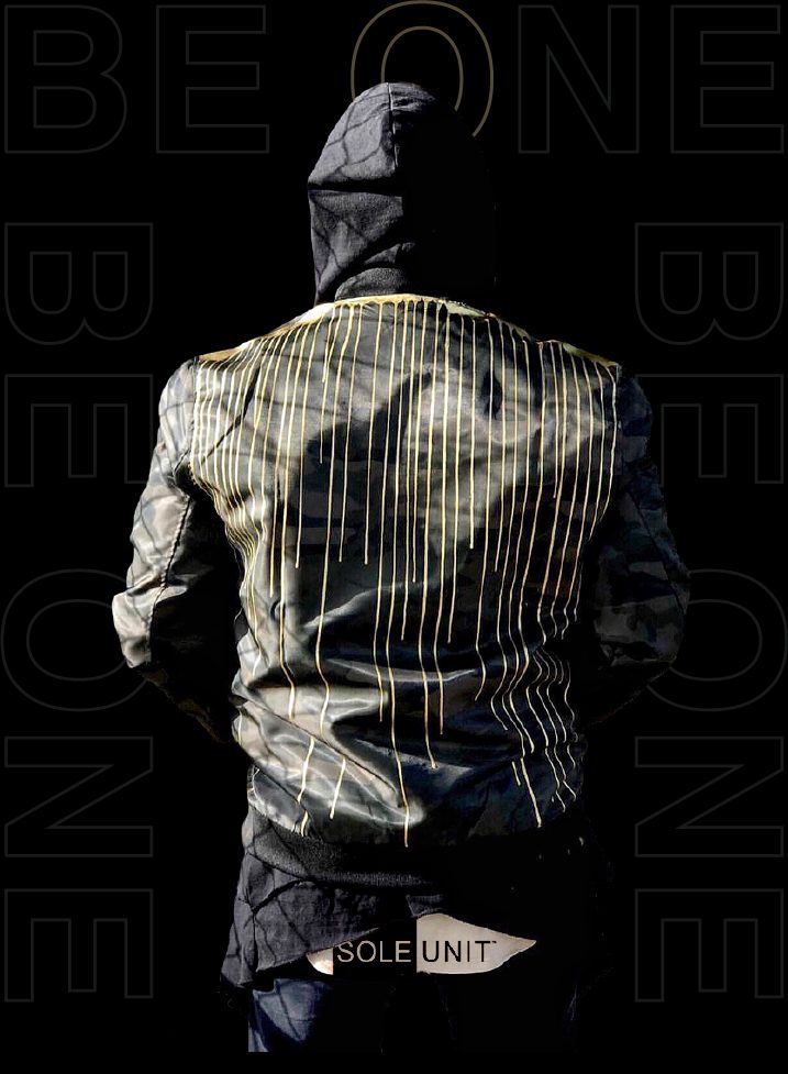 Camo jacket with gold drip print against repeated BE ONE outline type